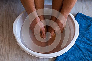 Male put hands and feet in bath with hot water and baking soda at home. Homemade bath soak for dry feet skin photo