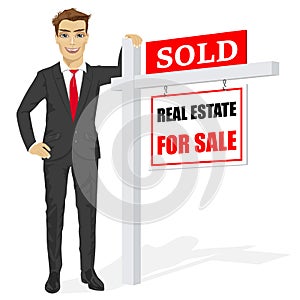 Male real estate agent standing next to a sold for sale sign