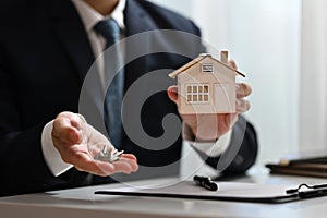 Male realtor or bank worker holding house model and keys. Real estate, loan and property investment concept