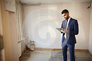 Male Realtor With Digital Tablet Carrying Out Valuation On Property For Renovation