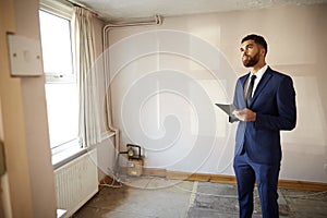 Male Realtor With Digital Tablet Carrying Out Valuation On Property For Renovation