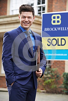Male Realtor Standing Outside Residential Property With Sold Sign