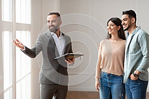 Male Realtor In Suit Showing Buyers New Apartment