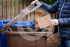 A male recycler placing a cardboard box into a brown roadside recycling bin photo