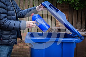 A male recycler placing a plastic bottle into a blue roadside recycling bin photo