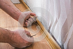 A male repairman installs a new baseboard in a house. Room renovation
