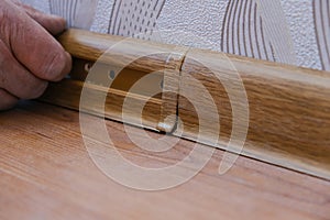 A male repairman installs a new baseboard in a house. Room renovation