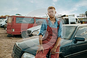 Male repairman poses on car junkyard