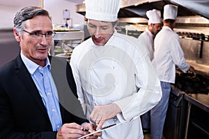 Male restaurant manager writing on clipboard while interacting to head chef