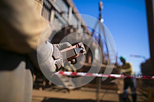 Male rigger hand controlling red hoist crane remote lifting load while blurry picture of his friend help holding stabilising the l