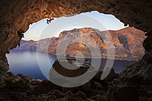 Male rock climber climbing along roof in cave before sunset.