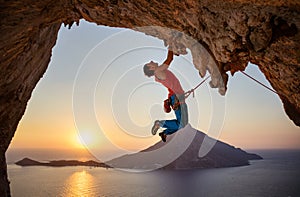 Male rock climber hanging with one hand on challenging route on cliff photo