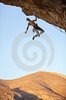 Male rock climber hanging with one hand on cliff