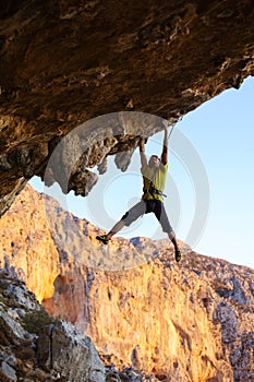 Male rock climber hanging on roof of cave