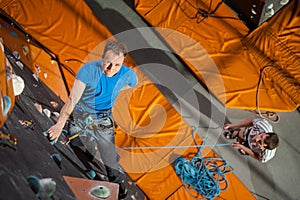 Male rock-climber practicing climbing on rock wall indoors