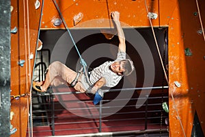 Male rock-climber practicing climbing on rock wall indoors