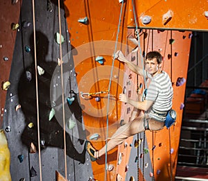 Male rock-climber practicing climbing on rock wall indoors