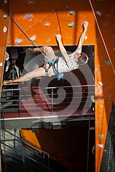 Male rock-climber practicing climbing on rock wall indoors