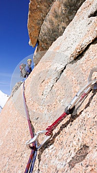 Male rock climbing a steep vertical granite rock climbing route in the French Alps near Mont Blanc above white snow glacier