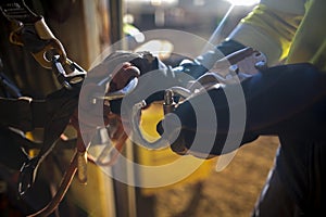 Male rope access hand wearing a glove is clipping descender which attached with locking carabiner into industry rope access harnes photo
