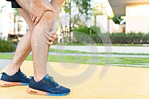 Male runner athlete leg injury and pain. Hands grab painful knee while running in the park