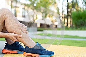 Male runner athlete leg injury and pain. Hands grab painful leg while running in the park