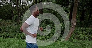 Male runner doing cardio workout on city park in morning. African man running outdoors. Tracking shot runner exercising