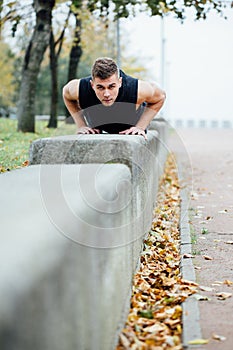 Male runner doing exercise, workout in the fall park. Push ups with bench.