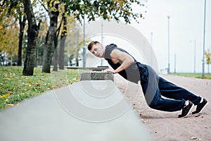 Male runner doing exercise, workout in the fall park. Push ups with bench.