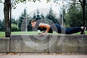 Male runner doing exercise, workout in the fall park. Push ups with bench.