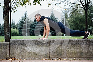 Male runner doing exercise, workout in the fall park. Push ups with bench.