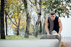 Male runner doing exercise, workout in the fall park. Push ups with bench.