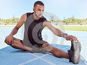 Male runner doing stretching exercises while sitting on sports track. Determined young male athlete sitting alone and