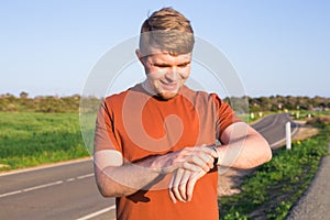 Male runner jogging outside looking at his wearable fitness tracker outside.