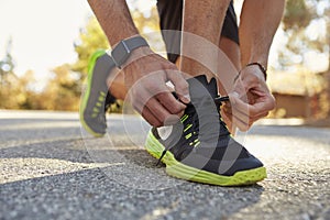 Male runner squatting in road tying his sports shoe close up