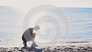 Male runner tying his shoelaces in the sun light on the beach slow motion