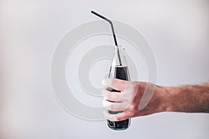 Male`s hand with bottle isolated over background. Tasty delicious sugary coke with plastic straw. Beverage carbonated