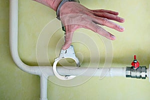 The male`s hand is handcuffed to a white heating pipe on a green background. A man`s hand reaches for the red tap. The concept o