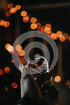 Male's hand holding a crystal ball with bokeh lights background
