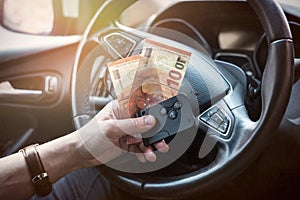 male's hand holding euro bills and key inside car for buy or rent