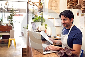 Male Sales Assistant Working On Laptop Behind Sales Desk Of Florists Store photo