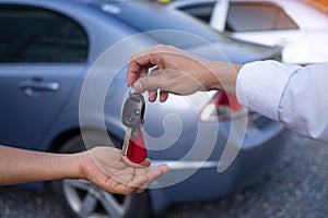 The male sales man is sending the keys and the car to the customer after agreeing to buy and sell the car.  Concept for car rental