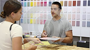 Male salesman of paintwork material shop advises woman buyer with samples and product catalog