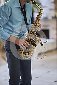 A male saxophonist in a blue shirt plays the saxophone.