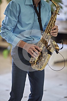 A male saxophonist in a blue shirt plays the saxophone.