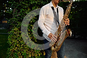 Male saxophonist plays on the alley in summer park