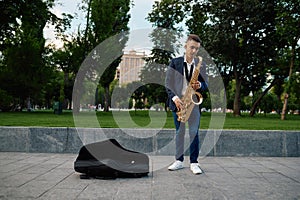 Male saxophonist plays melody in park, talent