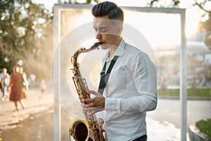 Male saxophonist plays melody on saxophone in park