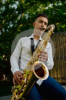 Male saxophonist plays the saxophone in park