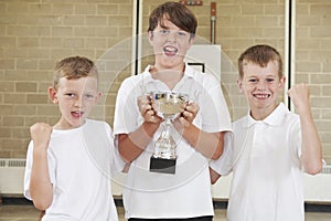 Male School Sports Team In Gym With Trophy